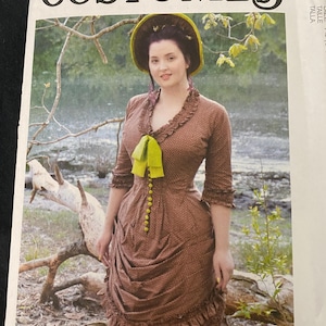 May include: McCall's Costumes pattern featuring a woman in a brown dress with a yellow bow and hat. The dress has a ruffled neckline and sleeves, with a fitted bodice and a gathered skirt. The pattern cover includes the text "Angela Clayton".