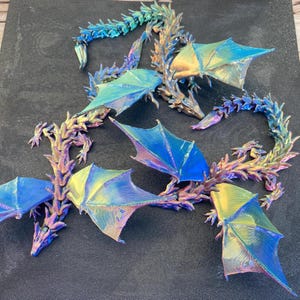 May include: Several iridescent dragon figurines with outstretched wings are displayed. The dragons have a detailed, textured appearance, with colors shifting from blue to gold and purple. The wings are a vibrant blue and yellow. The dragons are arranged on a dark surface.