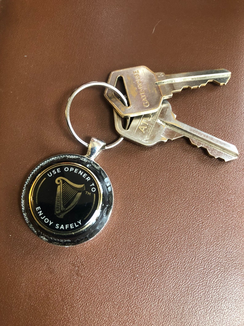 May include: A silver key chain with a black and gold round bottle opener. The bottle opener has the Guinness harp logo and the text "Use opener to enjoy safely".