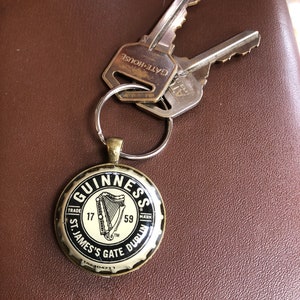 May include: A gold-colored bottle opener keychain with a black Guinness logo. The logo features a harp and the text "GUINNESS", "TRADE MARK", "17", "59", "ST. JAMES'S GATE DUBLIN".