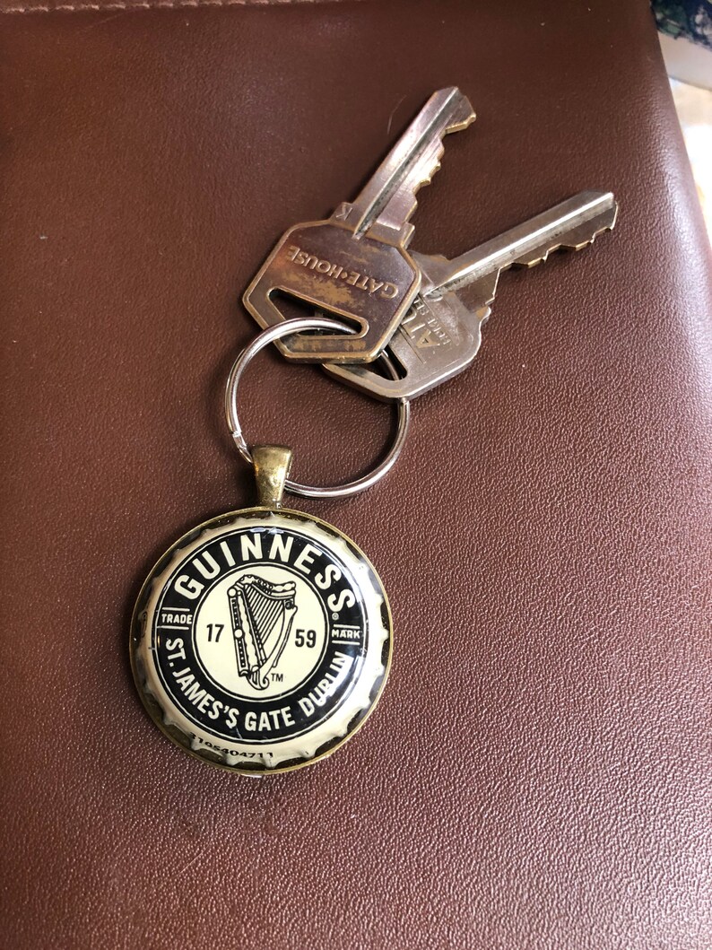 May include: A gold-colored bottle opener keychain with a black Guinness logo. The logo features a harp and the text "GUINNESS", "TRADE MARK", "17", "59", "ST. JAMES'S GATE DUBLIN".