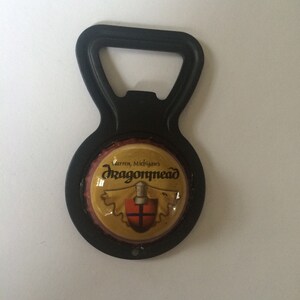 May include: Black bottle opener with a round, yellow and red Dragonmead logo. The logo says "Warren, Michigan's Dragonmead".
