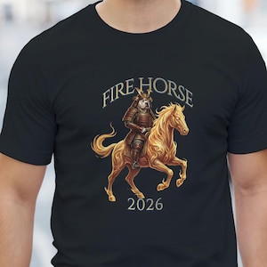 Könnte beinhalten: Schwarzes T-Shirt mit einer Grafik eines Samurai auf einem goldenen Pferd. Der Text "FIRE HORSE" steht über dem Bild, darunter "2026". Das T-Shirt wird von einer Person getragen.