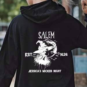 May include: Black hooded sweatshirt with a white graphic on the back. The graphic features the word "Salem" above an illustration of a witch, moon, and bats, with the text "EST. 1626" and "JESSICA'S WICKED NIGHT" below.