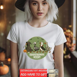 May include: White t-shirt featuring a Halloween-themed design with four cartoon geese dressed as a grim reaper, skeleton, vampire, and zombie. The text "GOOSEBUMPS NIGHT" is printed below the geese. A woman is wearing a black witch hat.