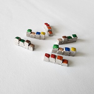 May include: Several small, rectangular, gray structures with colorful, stacked blocks on top. The blocks are painted in various colors, including red, orange, green, blue, and yellow. The objects are arranged on a white surface.
