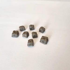 May include: A collection of eight small, gray, cube-shaped objects. Each cube has a textured surface, and they are scattered on a white background. The objects appear to be made of a solid material.