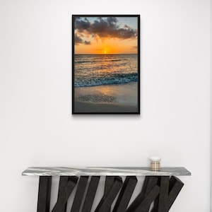 May include: A framed canvas print with a black frame. The image depicts a sunset over the ocean, with the sun setting on the horizon. The text "Canvas framed Black" is above the image.