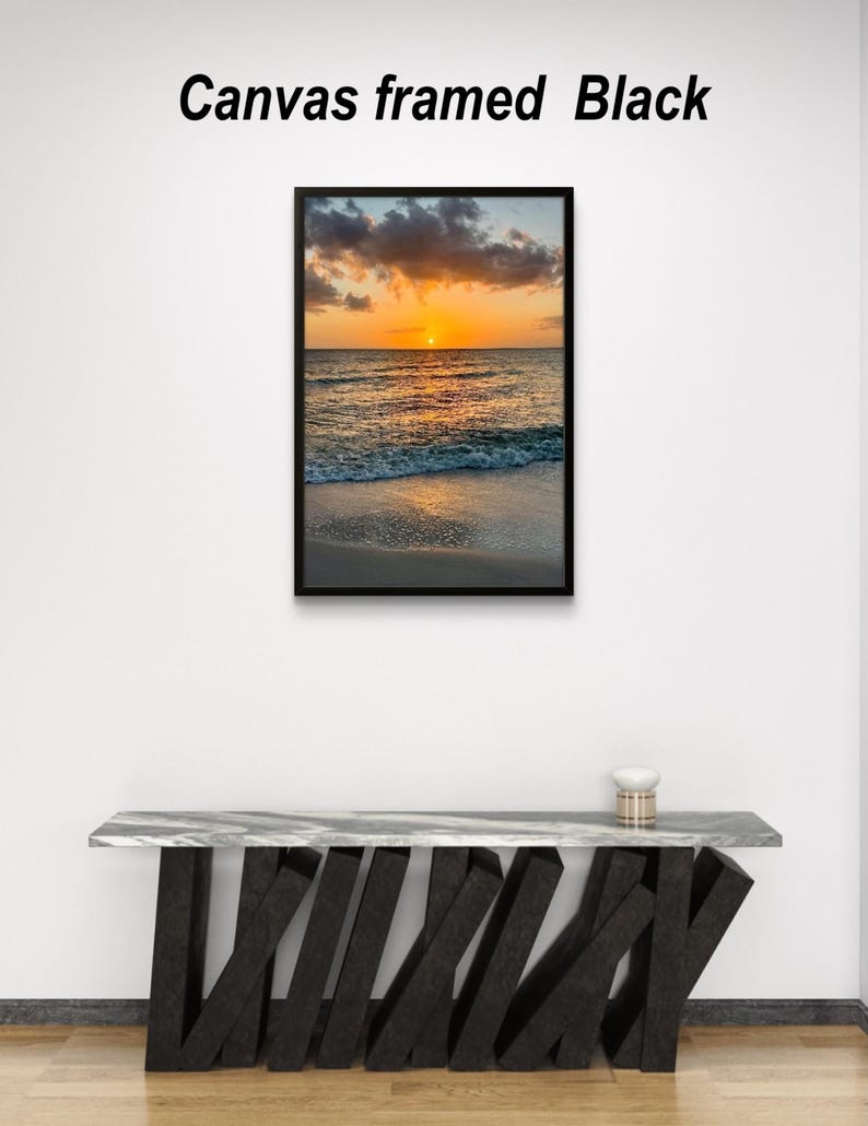May include: A framed canvas print with a black frame. The image depicts a sunset over the ocean, with the sun setting on the horizon. The text "Canvas framed Black" is above the image.