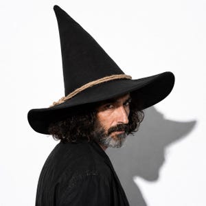 May include: A tall, pointed black hat with a wide brim, featuring a natural-colored twisted rope band wrapped around the base of the crown. The hat is constructed from a solid black material and maintains a structured, upright conical shape.