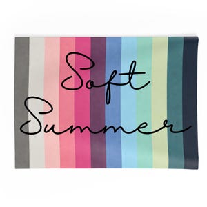 May include: A rectangular textile with vertical stripes in shades of gray, pink, purple, blue, and green. The words "Soft Summer" are written in cursive script across the center of the textile.