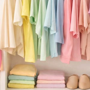 May include: A closet filled with pastel-colored clothing, including t-shirts, folded towels, and shoes. A rainbow-striped fabric and a straw handbag are also visible. The text reads: "Save time and dress with confidence."