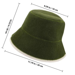 May include: An olive green bucket hat with a white underside and visible stitching. Dimension lines indicate a height of 10.22 inches, a top diameter of 6.29 inches, and a total width of 11.79 inches. The hat features a soft, felt-like texture.
