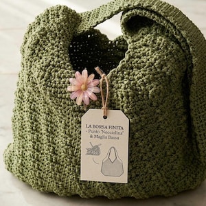 Può includere: Una borsa tote all'uncinetto verde oliva fatta a mano con un punto strutturato. Un fiore rosa e un'etichetta sono attaccati alla borsa. L'etichetta recita "LA BORSA FINITA - Punto 'Nocciolina' & Maglia Bassa" con un diagramma della borsa.