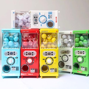 May include: A collection of colorful gumball machines in various colors, including blue, red, yellow, white, and green. Each machine is filled with gumballs and features a coin slot and dispensing mechanism. The machines have the words "COSMIC CODE" and "TWIZZLER SPACE" printed on them.