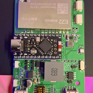 Op de afbeelding: Een groene printplaat met diverse elektronische componenten, waaronder een rechthoekige EBYTE-module met tekst en een QR-code, en een kleinere zwarte module. De printplaat bevat ook de tekst "WashTastic V0.3.5.5".