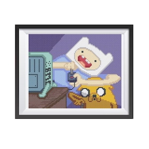 Op de afbeelding: Kruissteekkunstwerk met Finn en Jake uit Adventure Time. Finn, met een witte hoed en blauw shirt, houdt een controller vast. Jake, een gele hond, kijkt toe. De achtergrond is een paars, getextureerd patroon, alles in zwart omlijst.