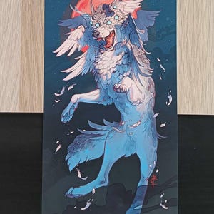 Könnte beinhalten: Illustration eines geflügelten Wolfes mit rotem Mond. Der Wolf ist blau und weiß, mit mehreren Flügeln und einem wilden Ausdruck. Federn schweben um den Wolf vor einem dunkelblauen Hintergrund und erzeugen eine dynamische Szene.