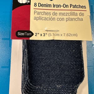 May include: A package of eight denim iron-on patches. The patches are dark blue and rectangular with rounded corners. The package includes the text "8 Denim Iron-On Patches" and the size is 2" x 3".
