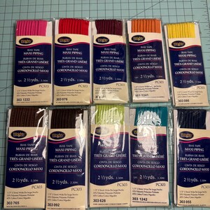 May include: A collection of ten packages of Wrights Maxi Piping bias tape in various colors, including pink, red, burgundy, orange, yellow, brown, dark brown, lime green, teal, and navy blue. Each package contains 2 1/2 yards of tape.