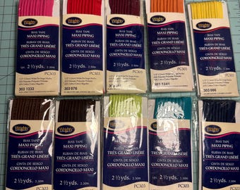 May include: A collection of ten packages of Wrights Maxi Piping bias tape in various colors, including pink, red, burgundy, orange, yellow, brown, dark brown, lime green, teal, and navy blue. Each package contains 2 1/2 yards of tape.