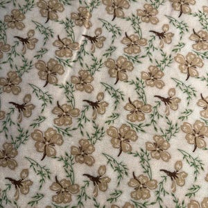 May include: Cream fabric featuring a repeating pattern of tan flowers and green vines. The flowers have five petals and are evenly spaced. The vines have small, pointed leaves, creating a floral design.