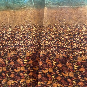 May include: A fabric panel featuring a beach scene. The top portion depicts a blue and turquoise ocean, transitioning to a sandy shore. The bottom half is covered in a detailed pattern of various-sized pebbles in shades of brown, tan, and gray.