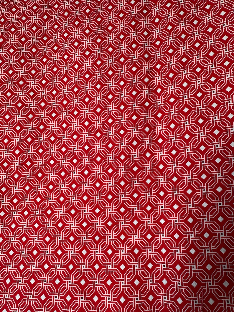 May include: Red fabric with a repeating geometric pattern of white interlocking shapes and diamond accents. The design creates a visually complex and symmetrical arrangement, suitable for various textile applications.