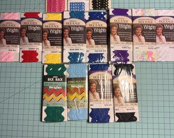 May include: A collection of colorful Rick Rack trim packages in various colors, including pink, red, yellow, blue, purple, and black. The packages are labeled with the "Wrights" brand and feature a woman's portrait. The trim is available in different lengths.