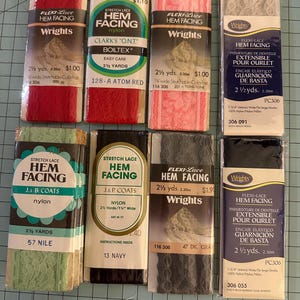 May include: Assortment of Flexi-Lace hem facing rolls in various colors, including red, pink, green, gray, and navy. Each roll is 2 1/2 yards long and features the Wrights brand. The packaging includes product information and pricing.