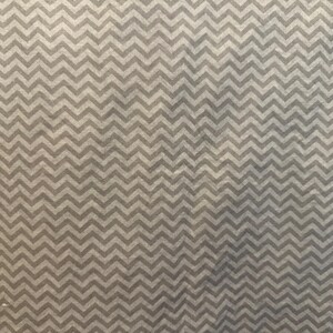 Peut inclure: Gros plan sur un tissu avec un motif de chevrons répété. Le motif est composé de zigzags gris clair et foncé, créant un aspect texturé. Le tissu a un aspect subtil et légèrement délavé.