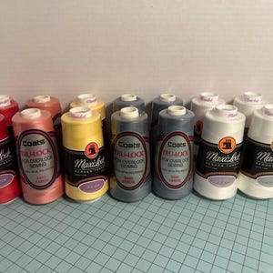 May include: A collection of Maxi-Lock and Coats Tru-Lock thread spools in various colors, including red, pink, yellow, gray, and white. The spools are labeled for overlock sewing and contain 3000 yards of spun polyester thread.