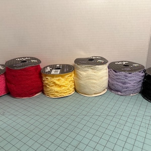 May include: A selection of ruffled lace spools in a range of colours: pink, red, yellow, cream, lavender, and black. Each spool is labelled with the brand name. The lace is suitable for sewing, crafting, or decorative projects.