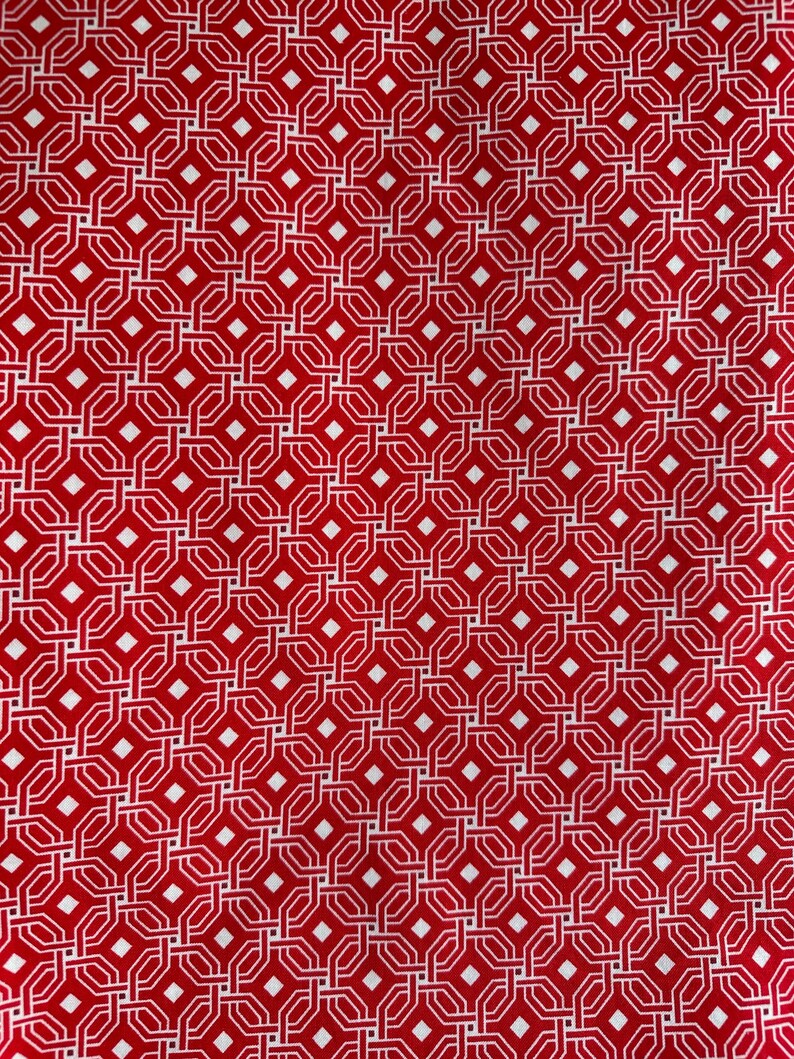 May include: A close-up of a red fabric with a repeating geometric pattern. The pattern consists of white interlocking shapes, including diamonds and octagons, creating a textured design. The fabric has a vibrant, saturated color.