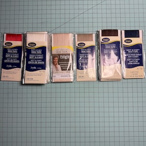May include: An overhead shot displays six packages of Wrights Soft & Easy Hem Tape in various colors. The packages are labeled with the product name, and each contains 3 yards of tape. Colors include red, white, beige, brown, and navy.