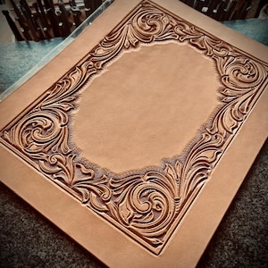 May include: A close-up of a light brown leather piece with an intricate, carved floral design around the border. The design is symmetrical and features a central blank space.