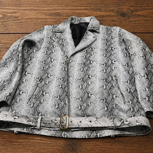 May include: A grey and black snakeskin-patterned jacket with a zip closure and a belt with a gold-coloured buckle. The jacket has a classic biker style with a notched collar and pockets.