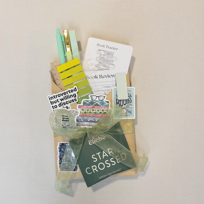 Puede incluir: Un juego de regalo con art&iacute;culos de papeler&iacute;a para amantes de los libros. Incluye bol&iacute;grafos, notas adhesivas, pegatinas y una bolsita de t&eacute; verde. El conjunto est&aacute; atado con una cinta verde y presenta el texto "introverted but willing to discuss" y "Star Crossed".
