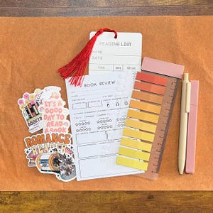May include: A reading list card with a red tassel, a book review form, two stickers with book-themed text and illustrations, a translucent ruler with a gradient of ten adhesive page markers in yellow and orange, and two pens in light pink and beige.