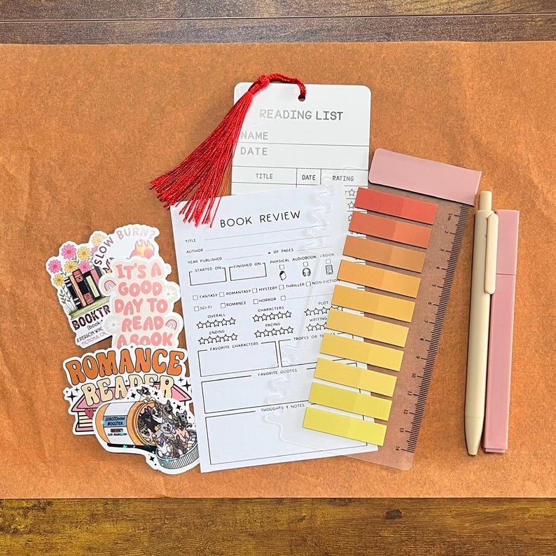 May include: A reading list card with a red tassel, a book review form, two stickers with book-themed text and illustrations, a translucent ruler with a gradient of ten adhesive page markers in yellow and orange, and two pens in light pink and beige.