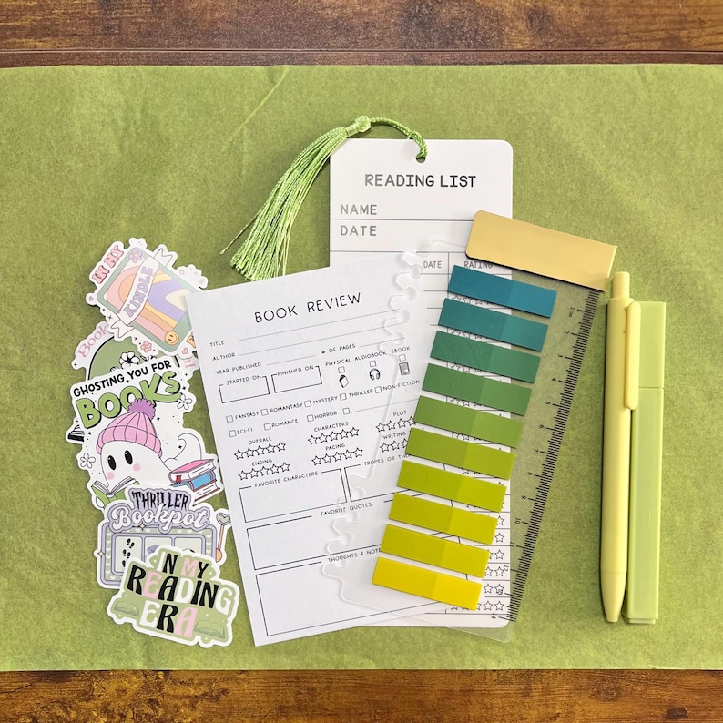 May include: A collection of stationery including a white reading list card with a green tassel, a book review card, a set of ten adhesive page markers in a green gradient on a clear ruler, and a yellow pen, alongside several decorative stickers.
