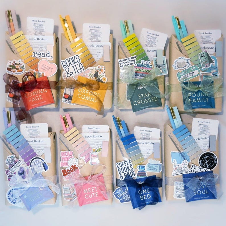 Puede incluir: Una colecci&oacute;n de regalos envueltos, cada uno adornado con pegatinas, bol&iacute;grafos y cintas decorativas. Los regalos presentan pegatinas tem&aacute;ticas de libros y texto como "Books & Tea" y "Coffee Books & Rain". Cada regalo incluye un bol&iacute;grafo y un marcap&aacute;ginas.