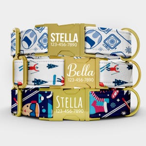 May include: Three dog collars stacked. The top collar has a white background with blue and white patterns. The middle collar has a white background with red and blue skiers. The bottom collar has a navy blue background with winter-themed graphics. Each collar has a gold buckle with a name and phone number.