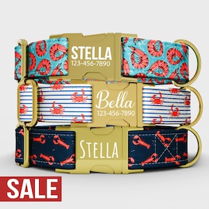 May include: Three personalised dog collars stacked. The top collar has a teal background with red prawns. The middle collar has blue and white stripes with red crabs. The bottom collar has a navy background with red lobsters. Each collar has a gold buckle with a name and phone number.