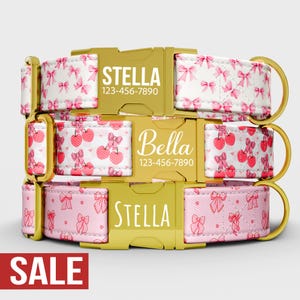 Puede incluir: Tres collares personalizados para perros con hebillas doradas. El collar superior es blanco con lazos rosas, el del medio tiene cerezas rojas y el inferior es rosa con lazos. Cada collar tiene un nombre y un número de teléfono.