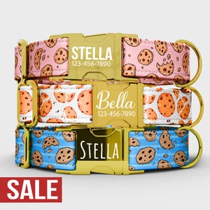 Puede incluir: Tres collares para perros con estampados de galletas en rosa, blanco y azul. Cada collar tiene una hebilla dorada con un nombre y un número de teléfono. La palabra "SALE" está en un rectángulo rojo en la parte inferior.