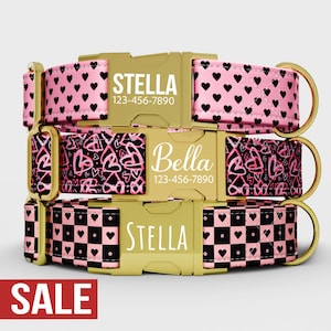 Puede incluir: Tres collares personalizados para perros con hebillas doradas. El collar superior es rosa con corazones negros, el del medio es negro y rosa con corazones, y el inferior es rosa y negro a cuadros con corazones. Cada collar tiene un nombre y un número de teléfono.