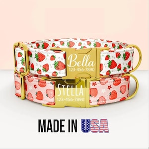 Op de afbeelding: Twee hondenhalsbanden met goudkleurige hardware. De bovenste halsband is wit met een aardbeienpatroon en de naam "Bella" op de gesp. De onderste halsband is roze met een aardbeienpatroon en de naam "Stella" op de gesp. De tekst "MADE IN USA" staat onderaan.