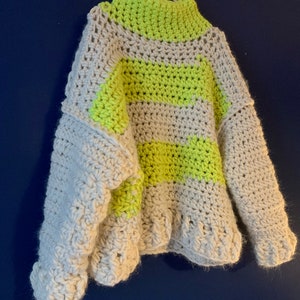 May include: A chunky crochet sweater featuring a high neckline and long sleeves. The garment is crafted from thick yarn in alternating horizontal stripes of off-white and vibrant neon yellow, showcasing a textured, hand-stitched knit pattern.