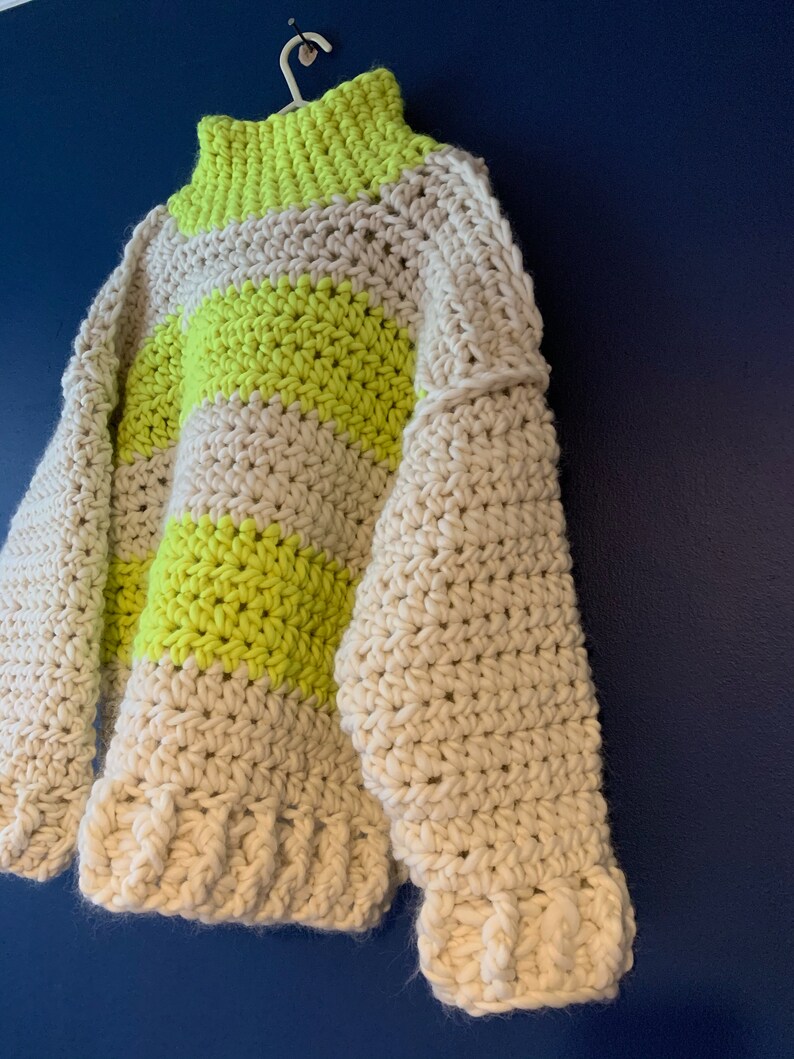 May include: A chunky crochet sweater featuring a high neck and long sleeves, crafted with thick yarn in alternating horizontal stripes of neon yellow and off-white. The garment has a textured, hand-stitched appearance with ribbed cuffs and hem.